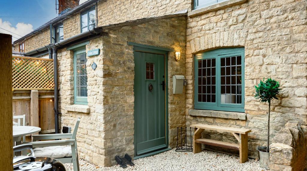 a stone house with a green door and a bench at Cedar Cottage in Chipping Norton