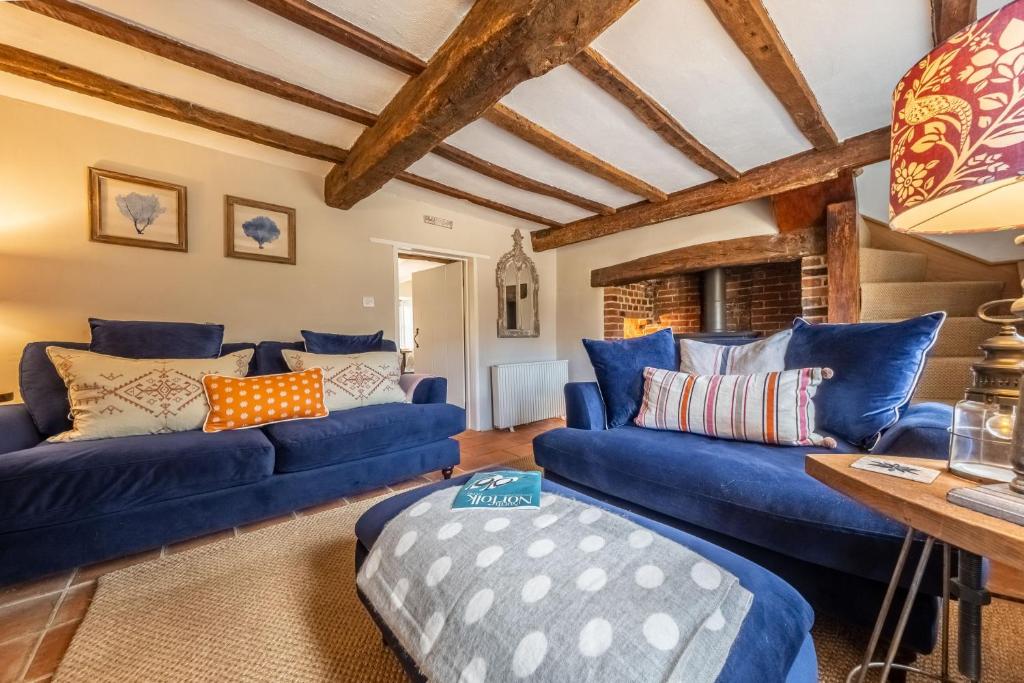 a living room with blue couches and wooden ceilings at Fox Cottage in South Creake
