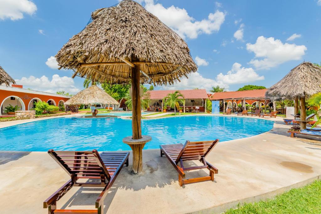 een zwembad met 2 stoelen en een rieten parasol bij Hacienda Inn in Mérida