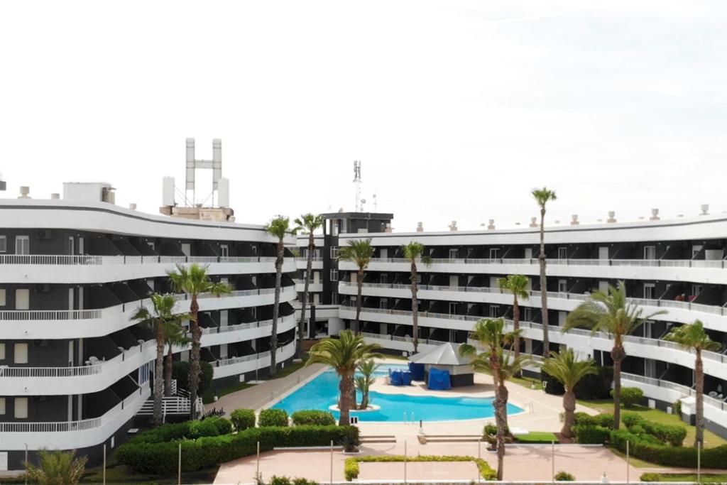 an apartment building with a swimming pool and palm trees at Palmera Beach in Pilar de la Horadada