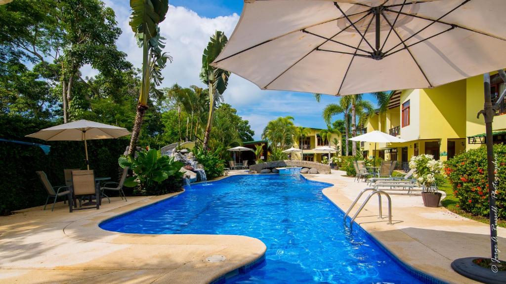 a swimming pool with an umbrella and tables and chairs at Club del Cielo Condominium Rental in Jacó