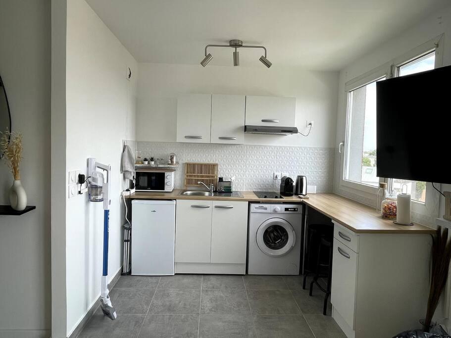cocina con armarios blancos, lavadora y secadora en appartement cosy et lumineux, en Orly