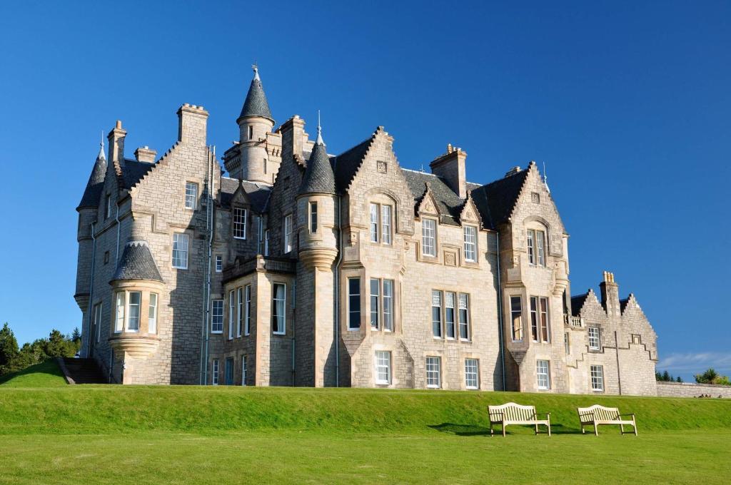 un vieux château avec deux bancs devant lui dans l'établissement Glengorm Castle, à Tobermory