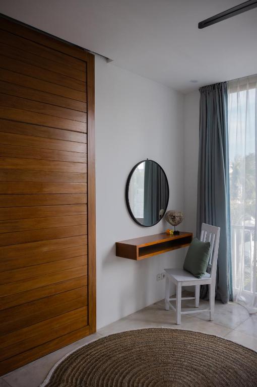 a bedroom with a wooden door with a chair and a mirror at The Bed by The Sea in Canggu