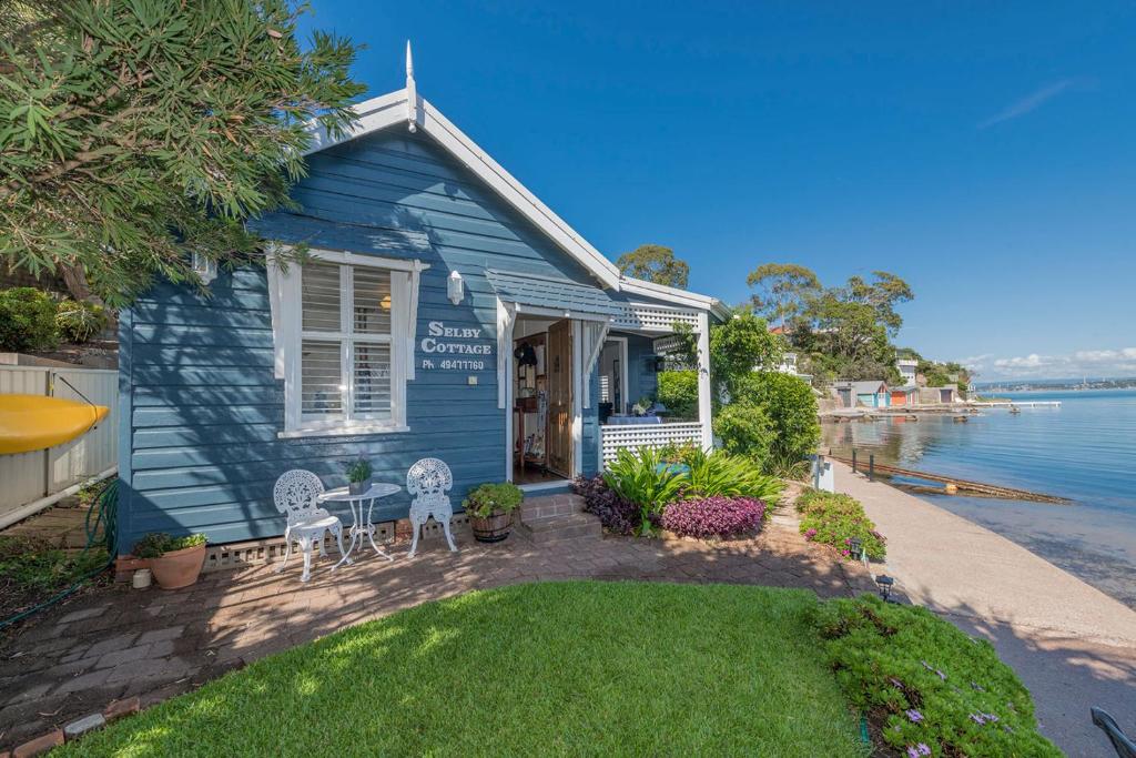 una casa azul con 2 sillas y un patio en Selby Cottage - Intimate Waterfront Getaway en Marks Point