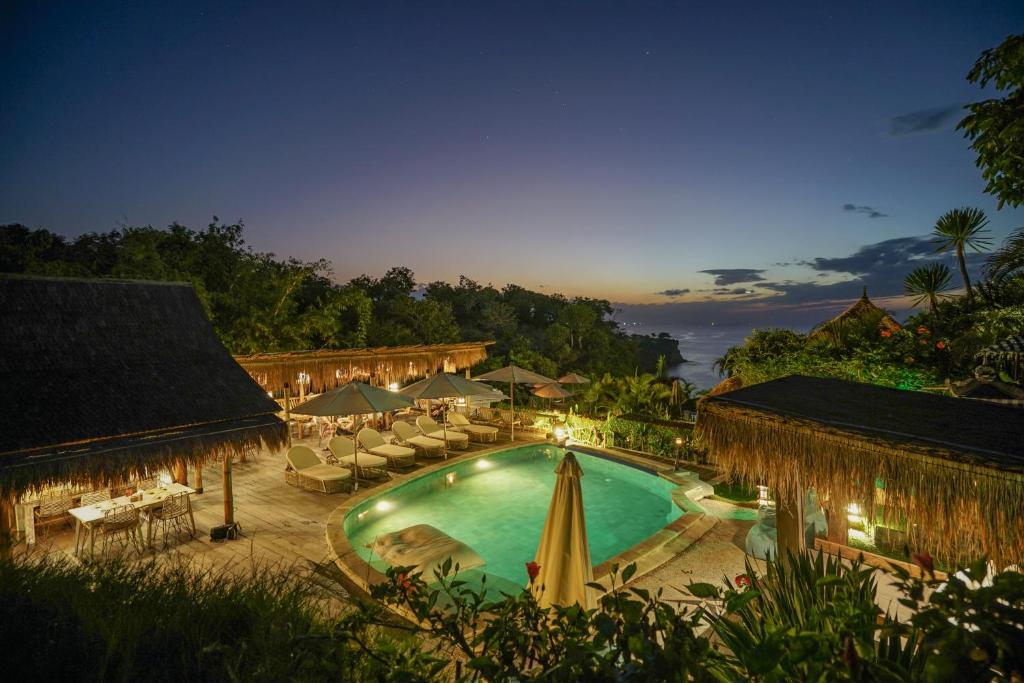 una piscina al aire libre con sillas y sombrillas por la noche en Milo's Home, en Jimbaran