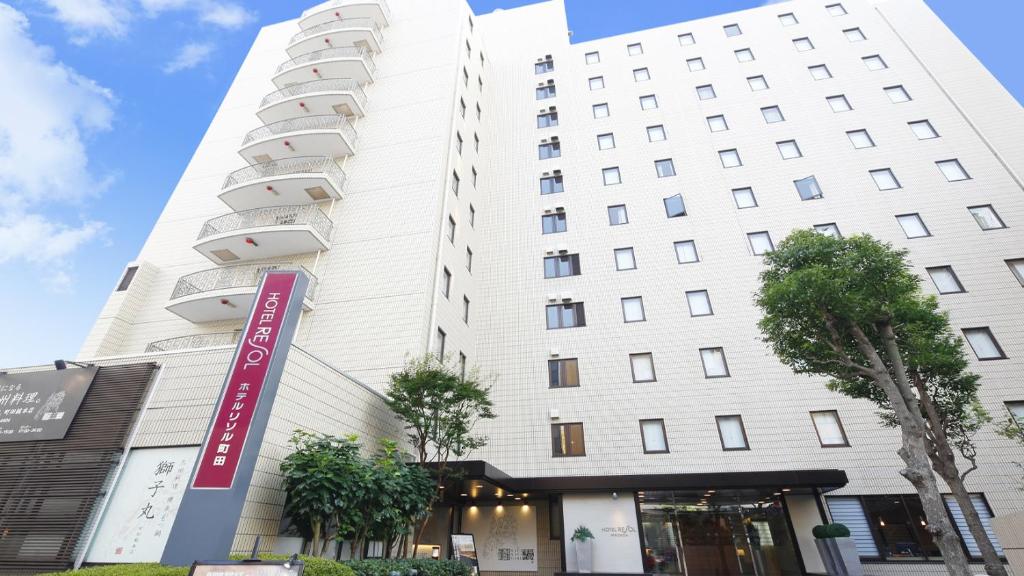un bâtiment blanc avec un panneau devant lui dans l'établissement Hotel Resol Machida, à Machida