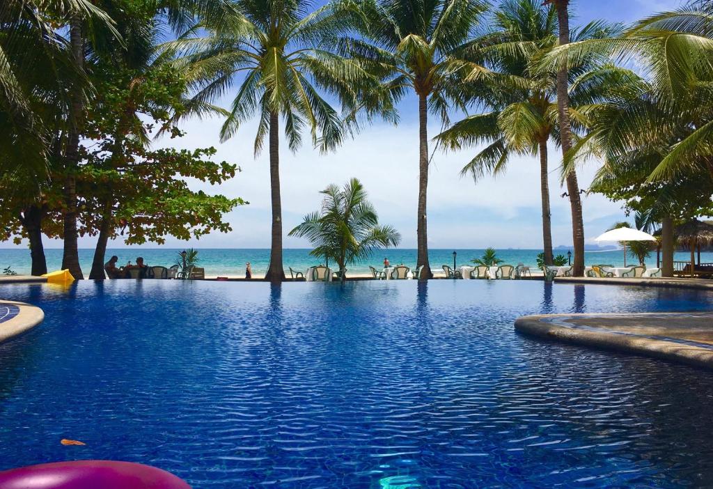 a swimming pool with palm trees and the ocean at Noble House Beach Resort in Ko Lanta