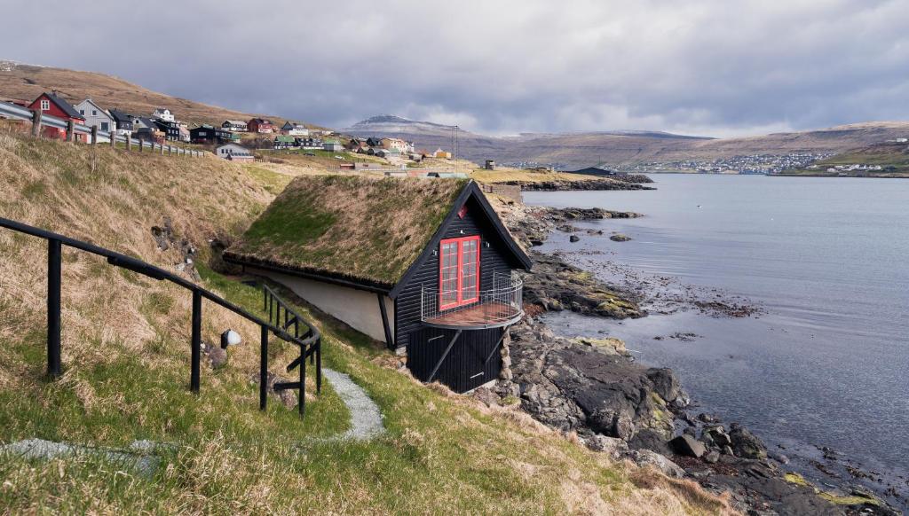 una casa con techo de hierba en una colina junto al agua en Unique boathouse by the foreshore / Sea view, en Strendur