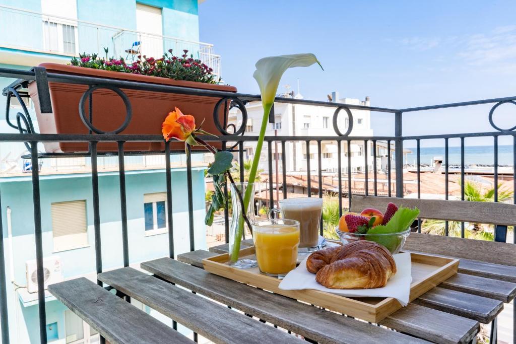 een tafel met een dienblad met brood en sap op een balkon bij Hotel Greta B&B in Rimini