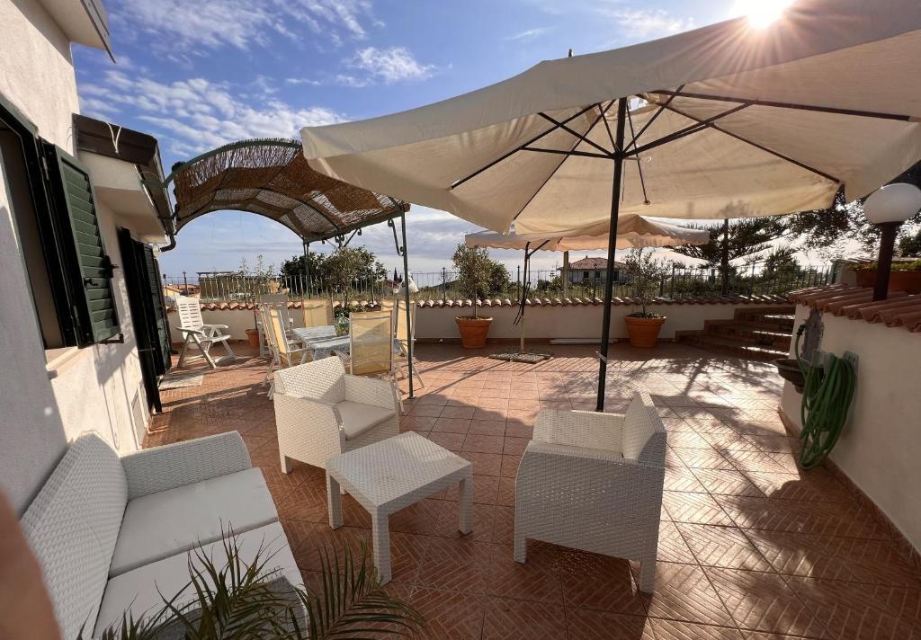 un patio con sillas blancas y una sombrilla en Villa Gina, en Marina di Fuscaldo