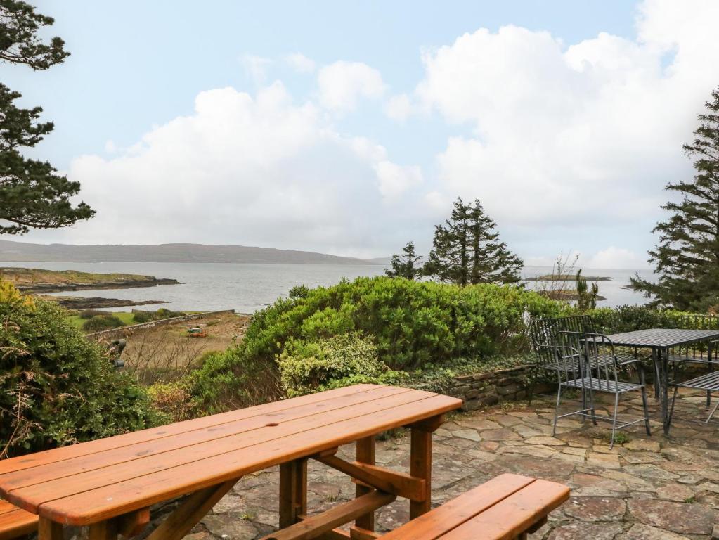 un banc en bois installé à côté d'une table et de l'océan dans l'établissement Whispering Pines, à Bantry