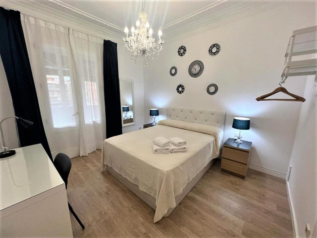 ein weißes Schlafzimmer mit einem Bett und einem Kronleuchter in der Unterkunft Flor Habitaciones in Barcelona