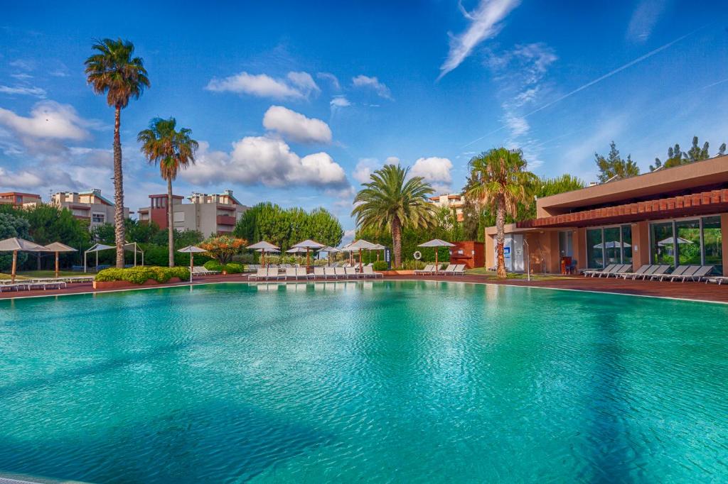 uma grande piscina com palmeiras e um edifício em Aqualuz Troia Mar by The Editory em Tróia