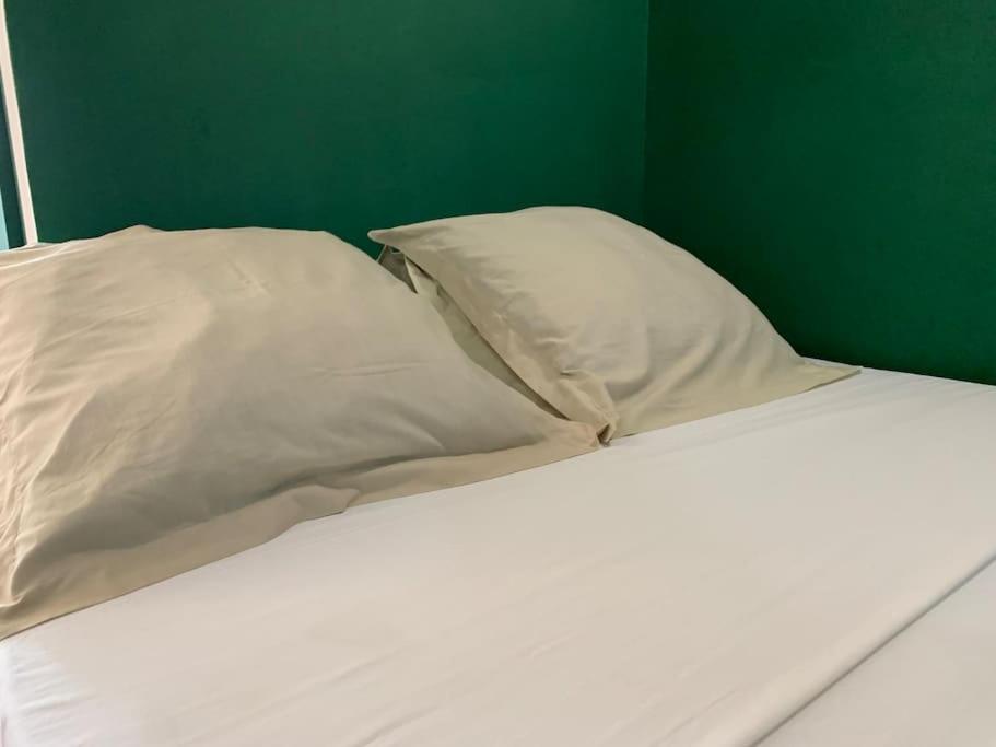 a white bed with two pillows and a green wall at Studio 19 Mamoudzou hyper centre in Mamoudzou