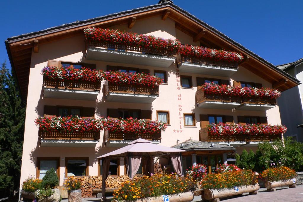 budynek z kwiatami na balkonach i parasolem w obiekcie Albergo du Soleil w mieście Cogne