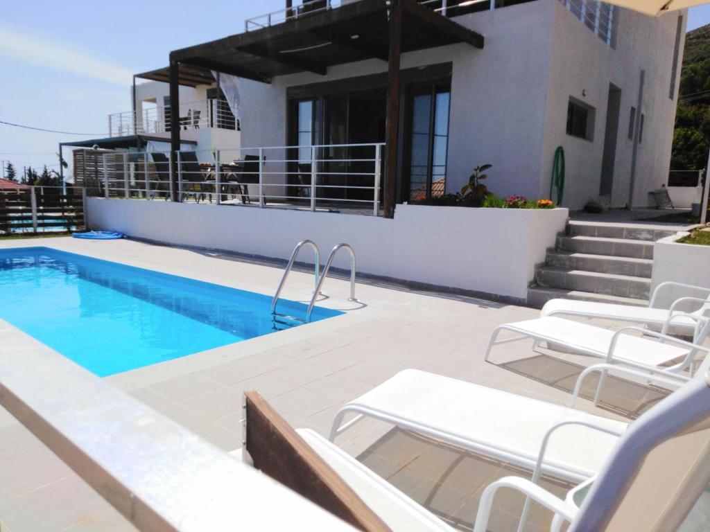 a swimming pool with white chairs and a house at Villa George sunrise in Ratzaklíon