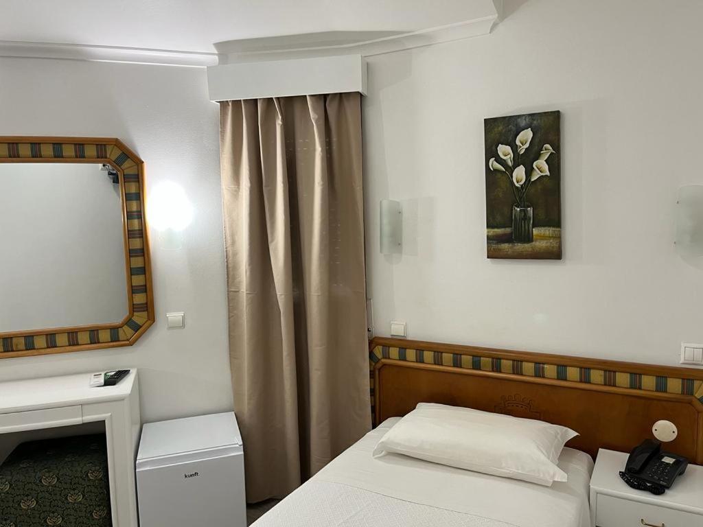 a small bedroom with a bed and a mirror at Real Caparica Hotel in Costa da Caparica