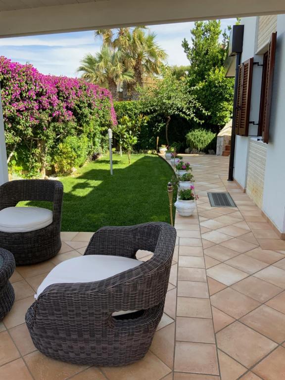 un patio con sillas de mimbre y césped con flores rosas en Villa MarLu en Bisceglie