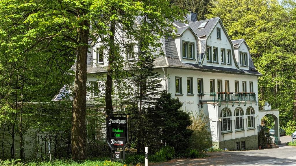 une grande maison blanche avec un panneau devant elle dans l'établissement Naturhotel Forsthaus, à Annaberg-Buchholz
