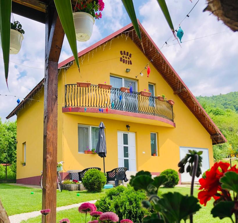 a yellow house with a balcony in a yard at Casa Sofia in Călimăneşti