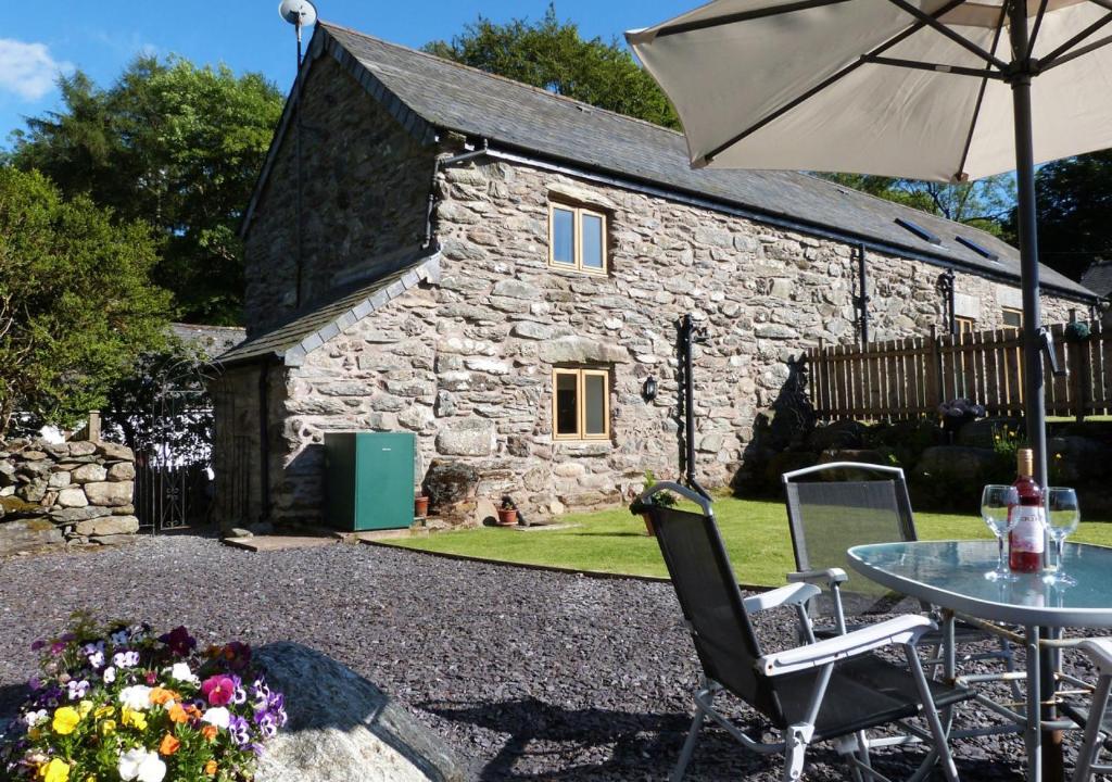 a stone cottage with a table and an umbrella at Crud y Wennol in Llandderfel