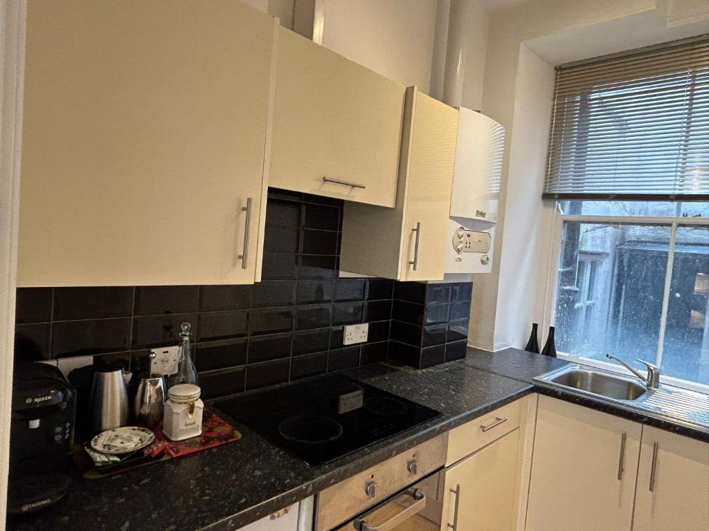 cocina con armarios blancos y encimera negra en John Street Apartments Flat 2 en Bristol