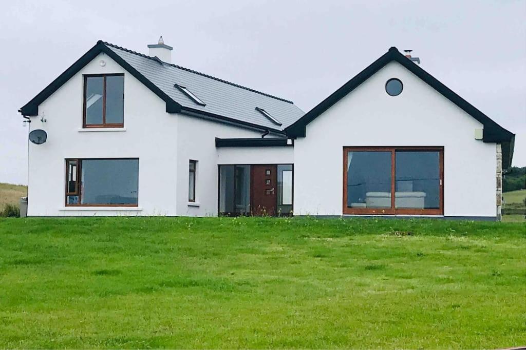 a white house with a black roof and green grass at Coast Lodge - Family vacation in Mulranny