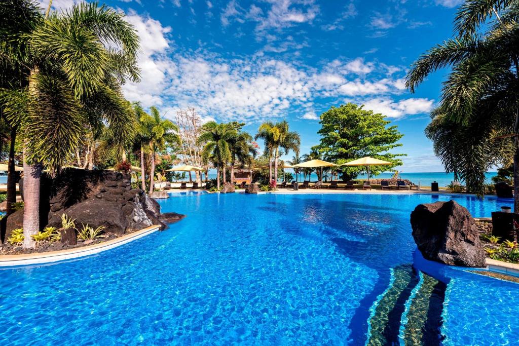 uma piscina com palmeiras e o oceano ao fundo em Sheraton Samoa Beach Resort em Mulifanua