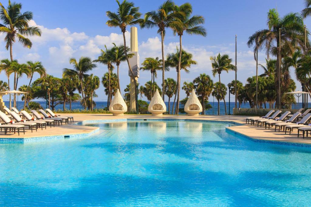 a swimming pool with chairs and palm trees at Renaissance Santo Domingo Jaragua Hotel & Casino in Santo Domingo