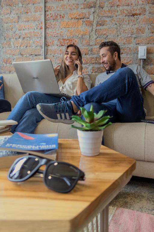 a man and woman sitting on a couch with a laptop at Ventiuna Hotel y Coliving in Pereira