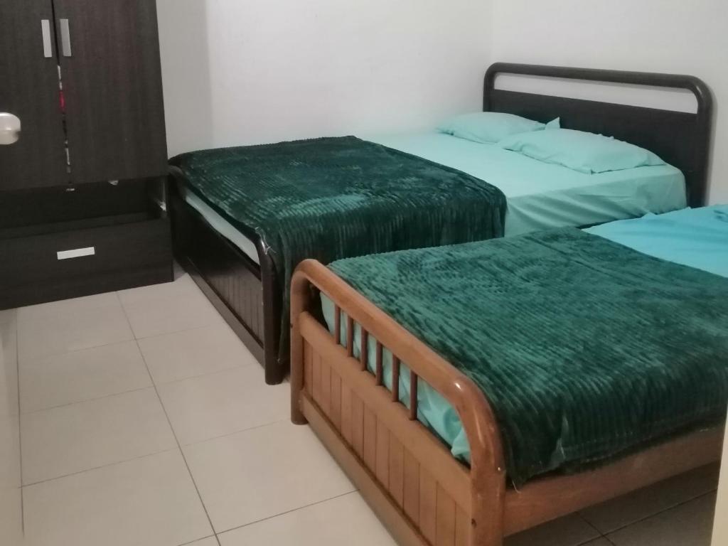 duas camas com lençóis verdes num quarto em Sis Homestay Wakaf Che Yeh, Kota Bharu em Kota Bharu