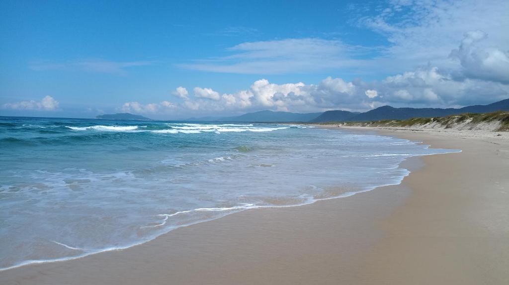 a sandy beach with the ocean and mountains in the background at Pousada ZAUA GUEST HOUSE in Florian&oacute;polis