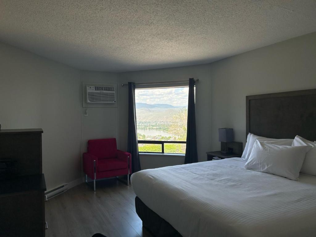a bedroom with a bed and a red chair and a window at The Vista Inn in Kamloops