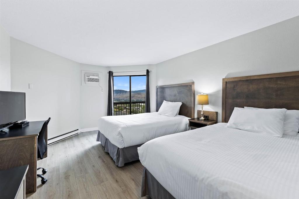 a hotel room with two beds and a desk and a television at The Vista Inn in Kamloops