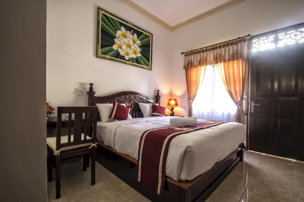 a bedroom with a bed and a chair and a window at Frangipani Homestay in Nusa Dua