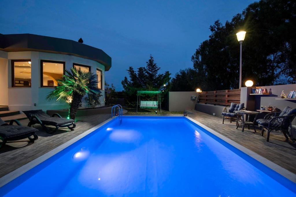 a blue swimming pool in a backyard at night at Maia Luxury Pool Villa in Afantou