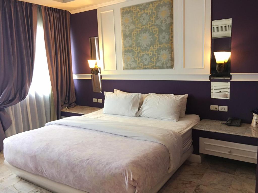 A purple-accented bedroom with a large bed, heavy curtains and bedside storage.