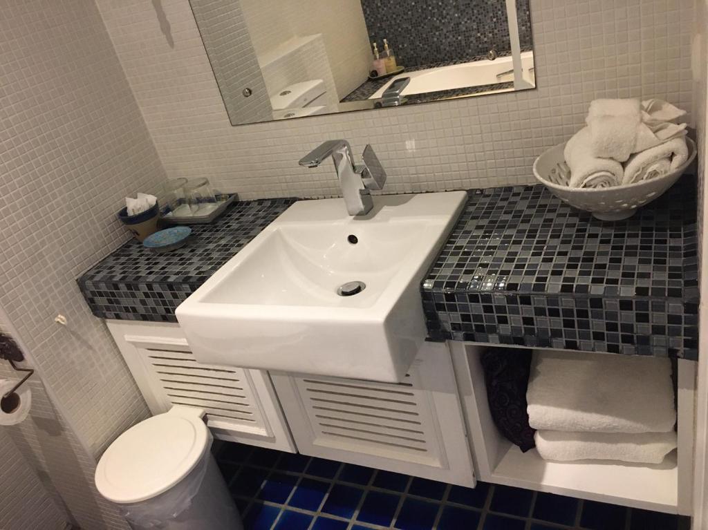 A compact vanity with a basin, mosaic countertop and open towel storage.
