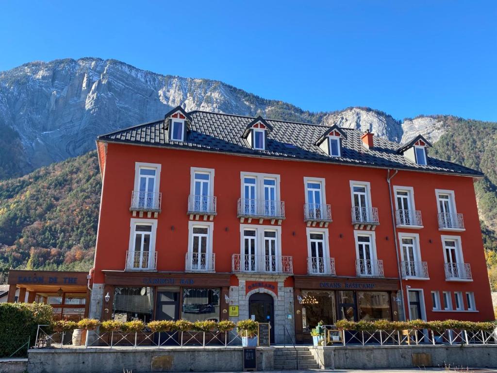 a red building with a mountain in the background at hôtel oberland in Le Bourg-dʼOisans