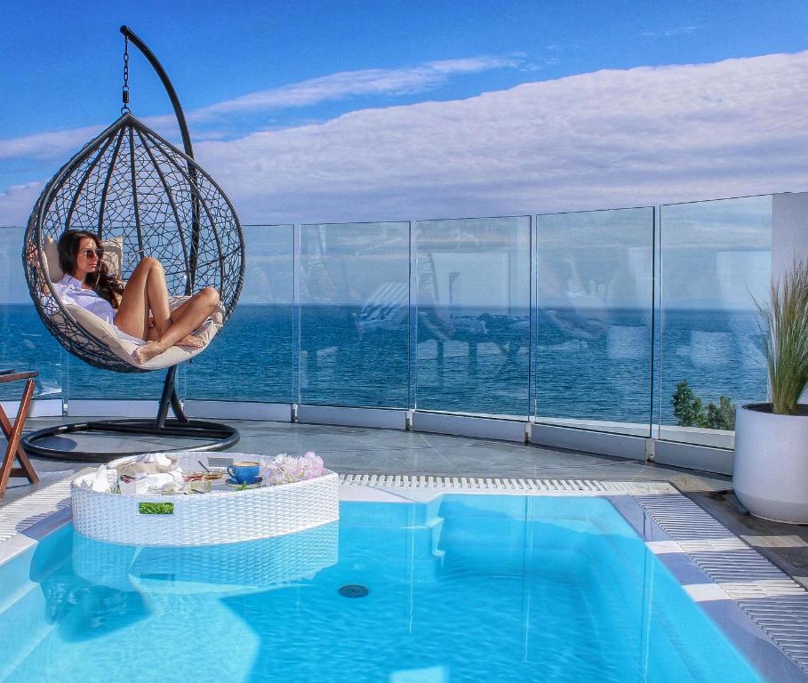a woman sitting in a swing next to a swimming pool at Panorama Suites & Spa - Adults Only in Stomio