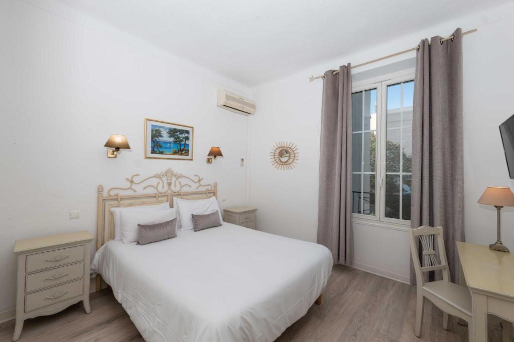 a white bedroom with a bed and a desk and a window at Hôtel Beau Site - Cap d'Antibes in Antibes