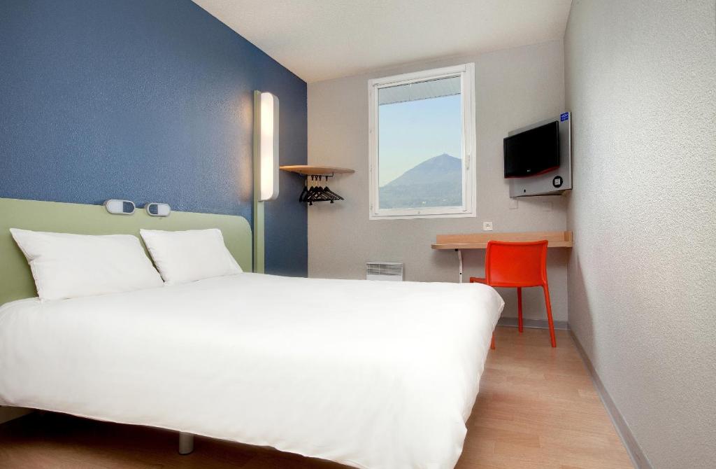 um quarto com uma cama branca, uma mesa e uma janela em ibis budget Clermont Ferrand Nord Riom em Riom