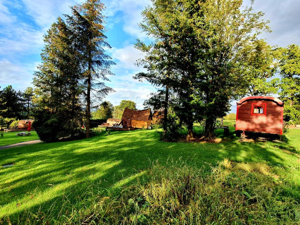 un pequeño cobertizo en un campo de hierba con árboles y una casa en les Refuges du Chalet, en Sart-lez-Spa