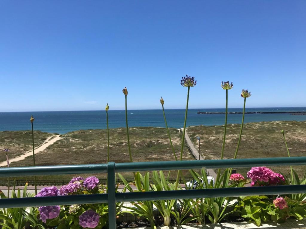 Beachfront Apartment With Sea View في Azurara: سور به الزهور والمحيط في الخلفية