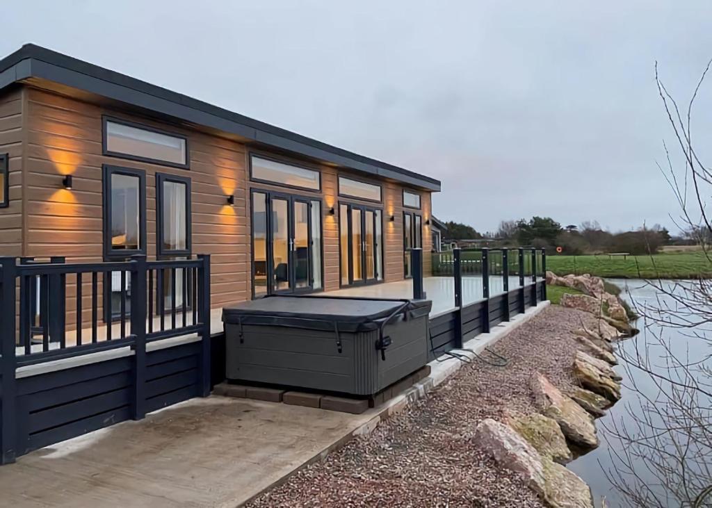 a tiny house with a large deck next to a body of water at Gorgeous Lake Lodge with HTub Outstanding Views in Annan