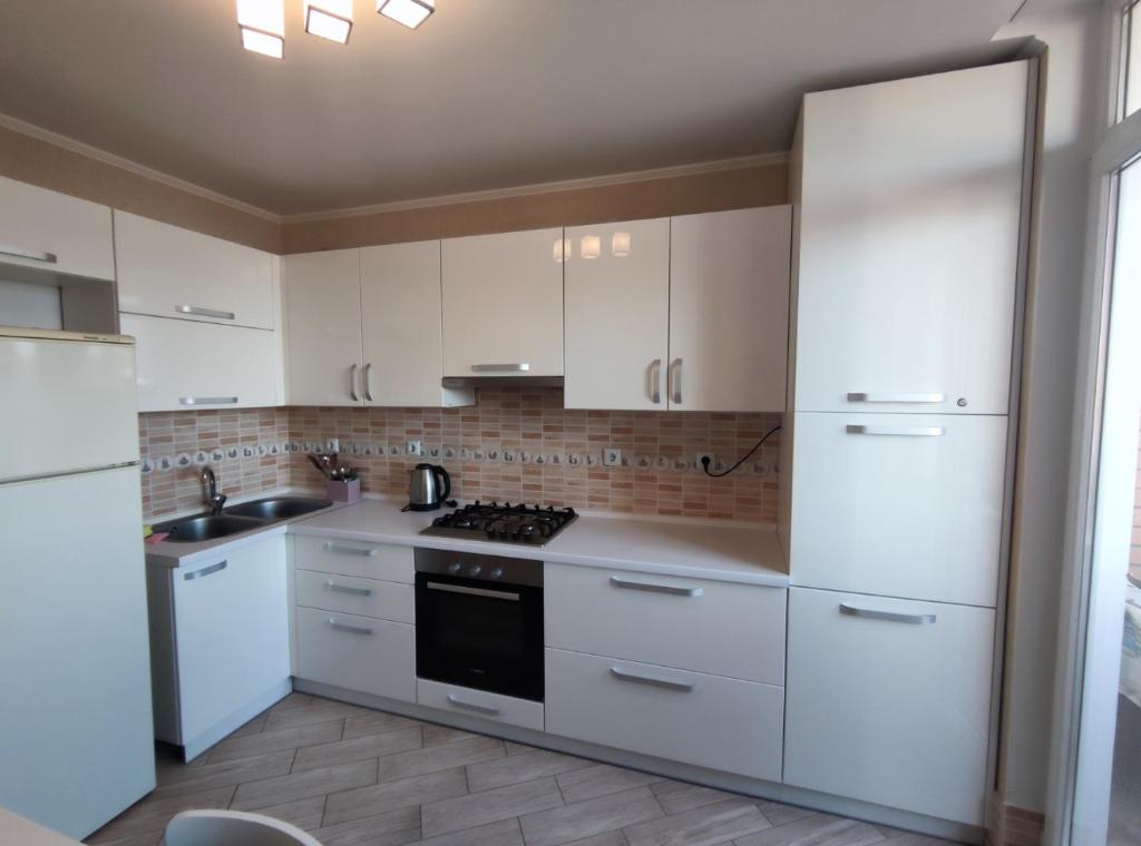 La cuisine est équipée de placards blancs et d'un four avec plaques de cuisson. dans l'établissement 2-х кімн квартира в новобудові, à Ternopil