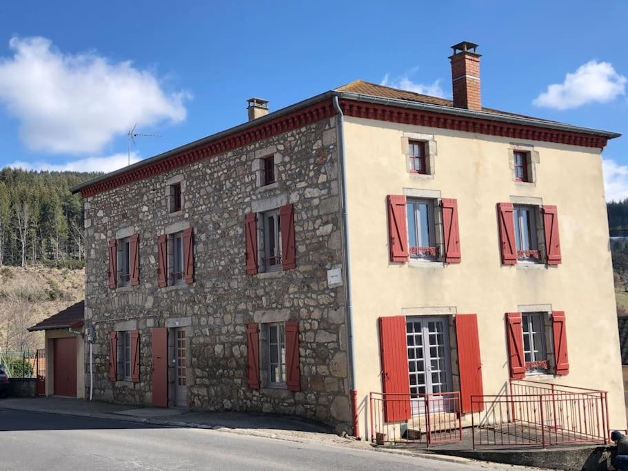 um antigo edifício de pedra com persianas vermelhas numa rua em Le Val Danse - Maison de caractère de 1870 - Rénovée en 2020 em Saint-Anthème