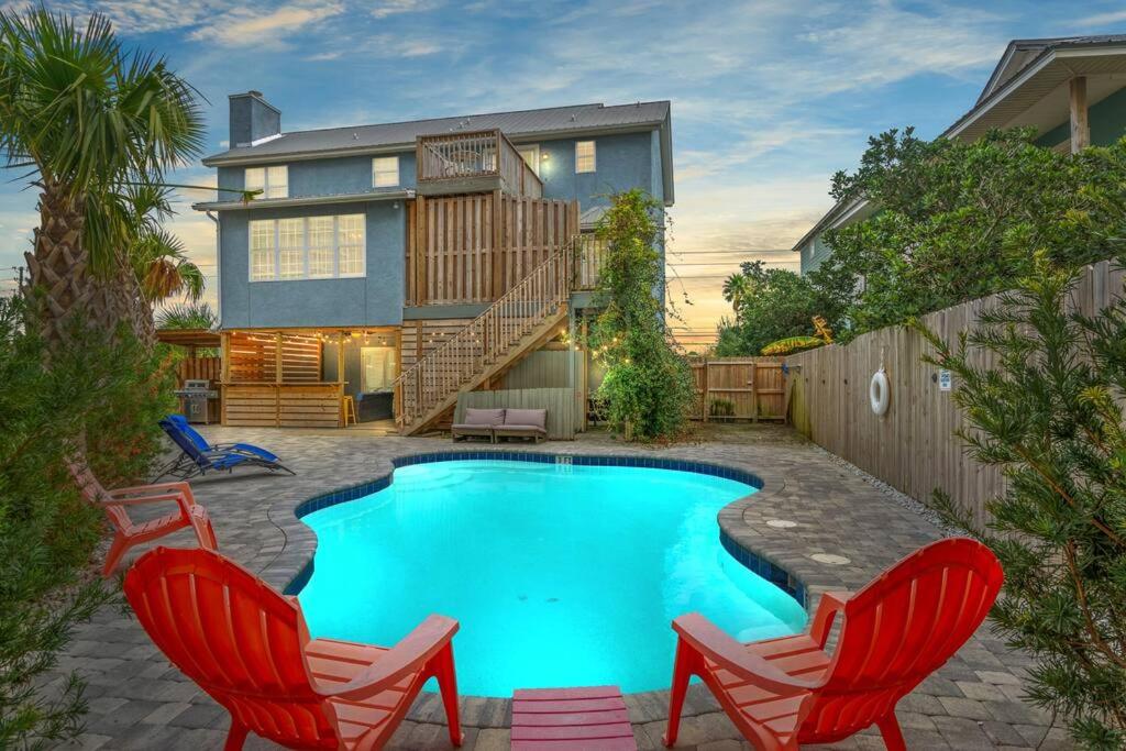 a swimming pool with two chairs and a house at Sand Castle-Pool, Game Rooms, covered outdoor space with tiki bar, 1min walk to beach in Panama City Beach