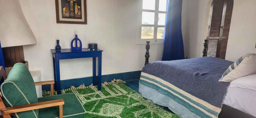 a bedroom with a bed and a chair and a table at Hotel-Restaurant Le Kaouki in Sidi Kaouki